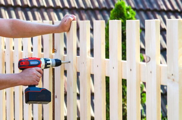 Person using a cordless drill on a wooden fence.