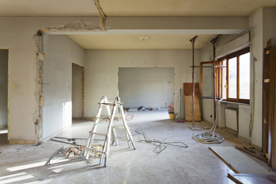 Interior of a room under renovation with exposed pipes and electrical wires, a ladder, and construction debris.