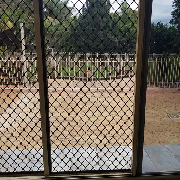 View through a screen door showing a paved patio and a metal fence.